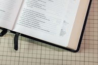 An open book with handwritten verses and a quill pen beside it.