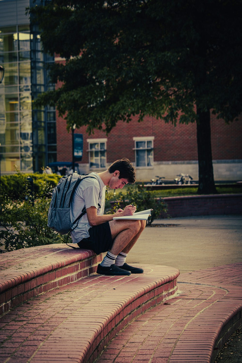 a man sitting on a brick sidewalk reading a book