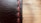 A close-up view of a black leather surface with prominent red stitching running vertically. The texture of the leather is visible, with fine lines and slight imperfections giving it a rugged look. The background is softly blurred, creating a warm contrast with the leather's dark hue.