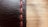 A close-up view of a black leather surface with prominent red stitching running vertically. The texture of the leather is visible, with fine lines and slight imperfections giving it a rugged look. The background is softly blurred, creating a warm contrast with the leather's dark hue.
