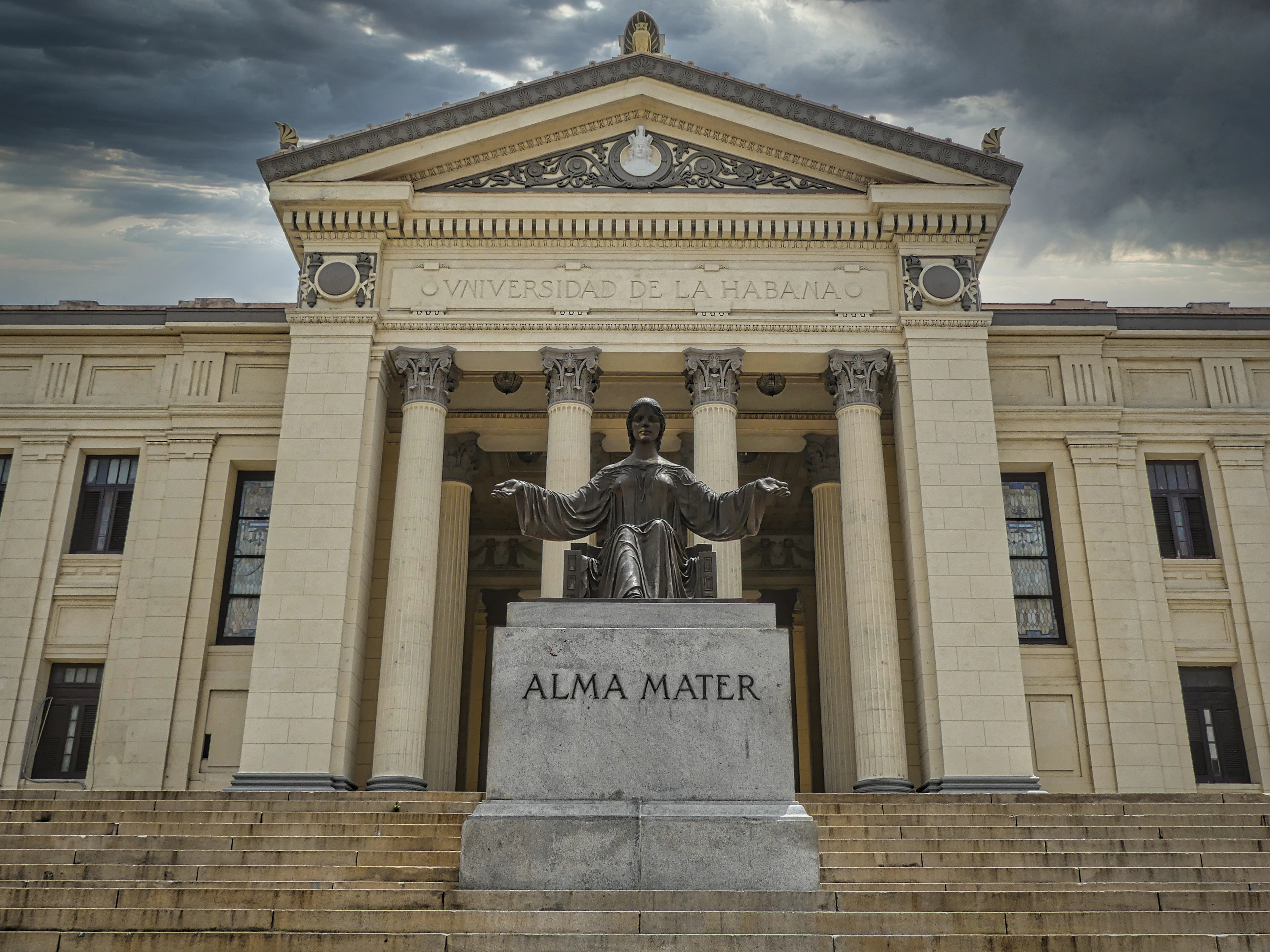 Stone steps lead up to the University of Havana's Alma Mater statue under a stormy sky.