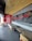 A modern fast-food restaurant interior features wooden ceiling slats, red and black decor, and seating arrangements with beige chairs and black tables. Red neon signage and a decorative wall display add to the ambiance.