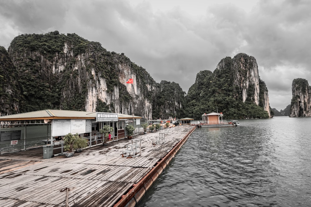 a dock leading to a building by a body of water with mountains in the background