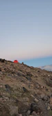 Traditional Bedouin tents nestled at the base of rocky hills under a vast blue sky.