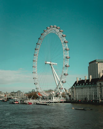 a ferris wheel by water with London Eye in the background
