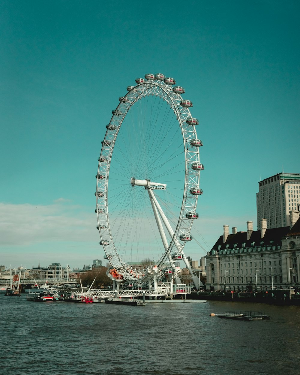a ferris wheel by water with London Eye in the background