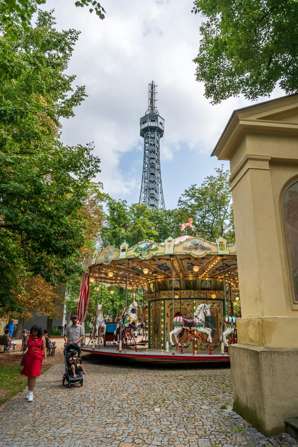 a group of people walking around a park with a tower in the background