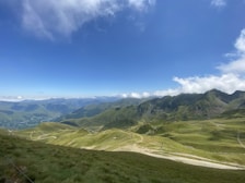 View of a mountain trail winding through green hills under a bright blue sky
