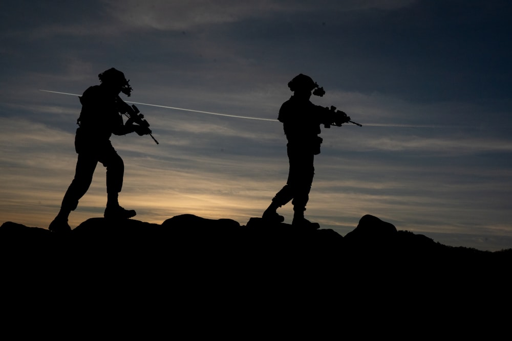 a couple of men walking on a hill with guns