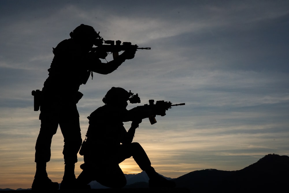 silhouette of a couple of people holding guns