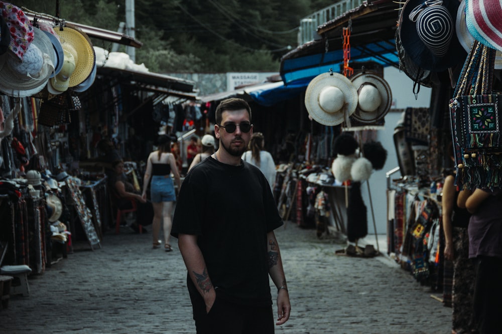 a man standing in front of a street with many hats on it