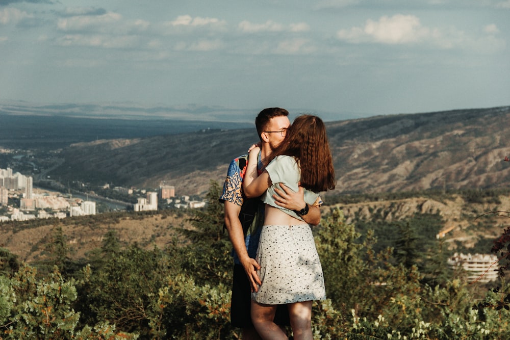 a man and woman hugging on a hill overlooking a city