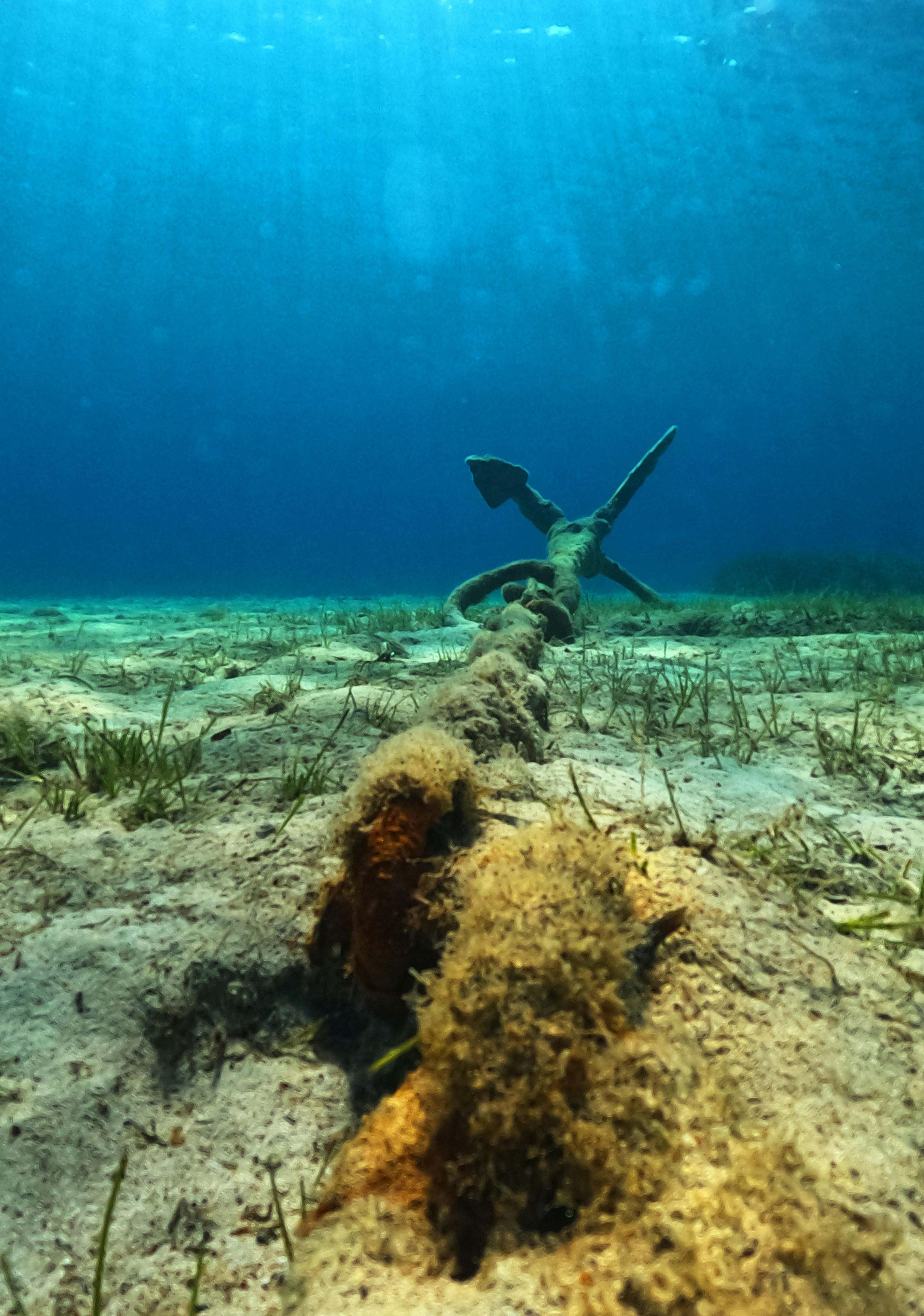 Anchor resting on sandy ocean floor with rays of light filtering through calm blue water