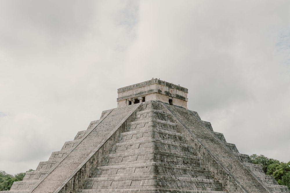 a stone pyramid with a cloudy sky with Chichen Itza in the background