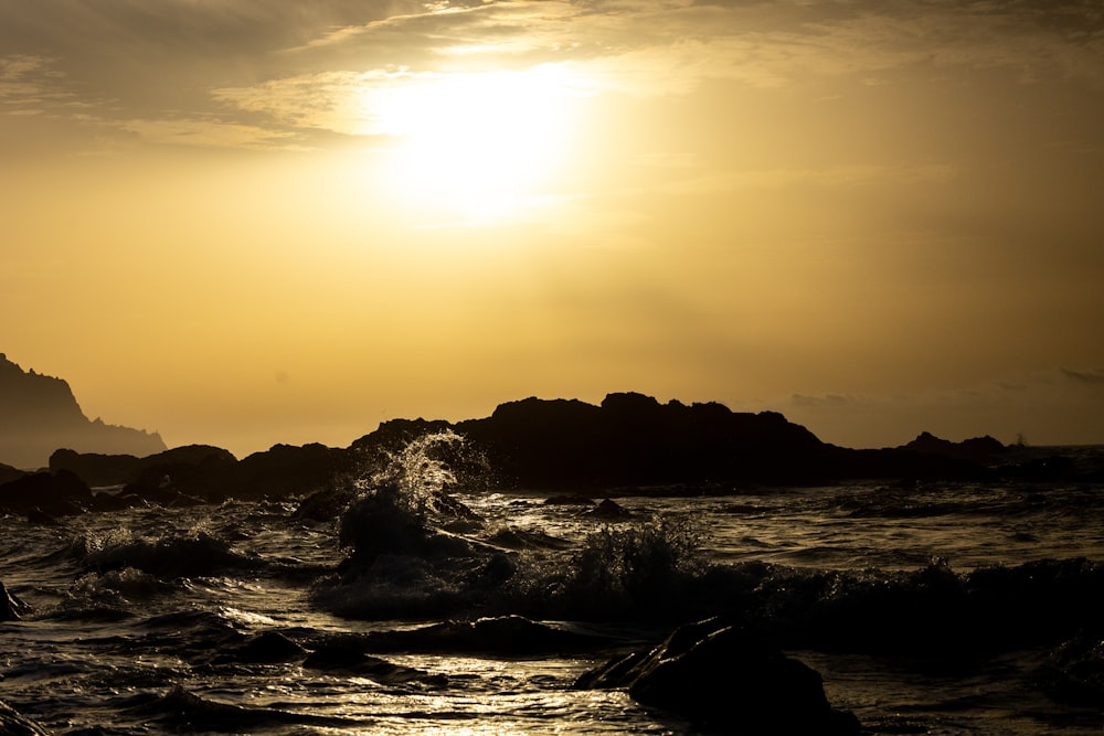 a body of water with waves and rocks and a sunset