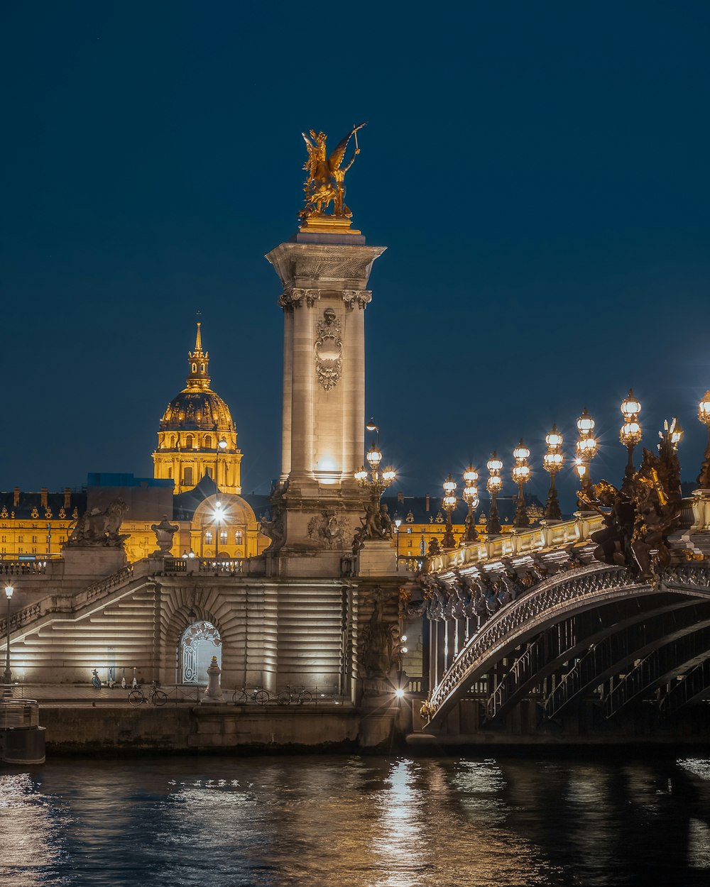 a statue on a pillar in front of a bridge with a gold and blue building in the background