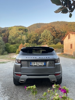 A Range Rover cruising along a gravel path bordered by rolling green fields under a cloudy sky.