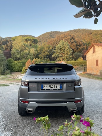 A Range Rover driving along a gravel road surrounded by lush hills and open sky.