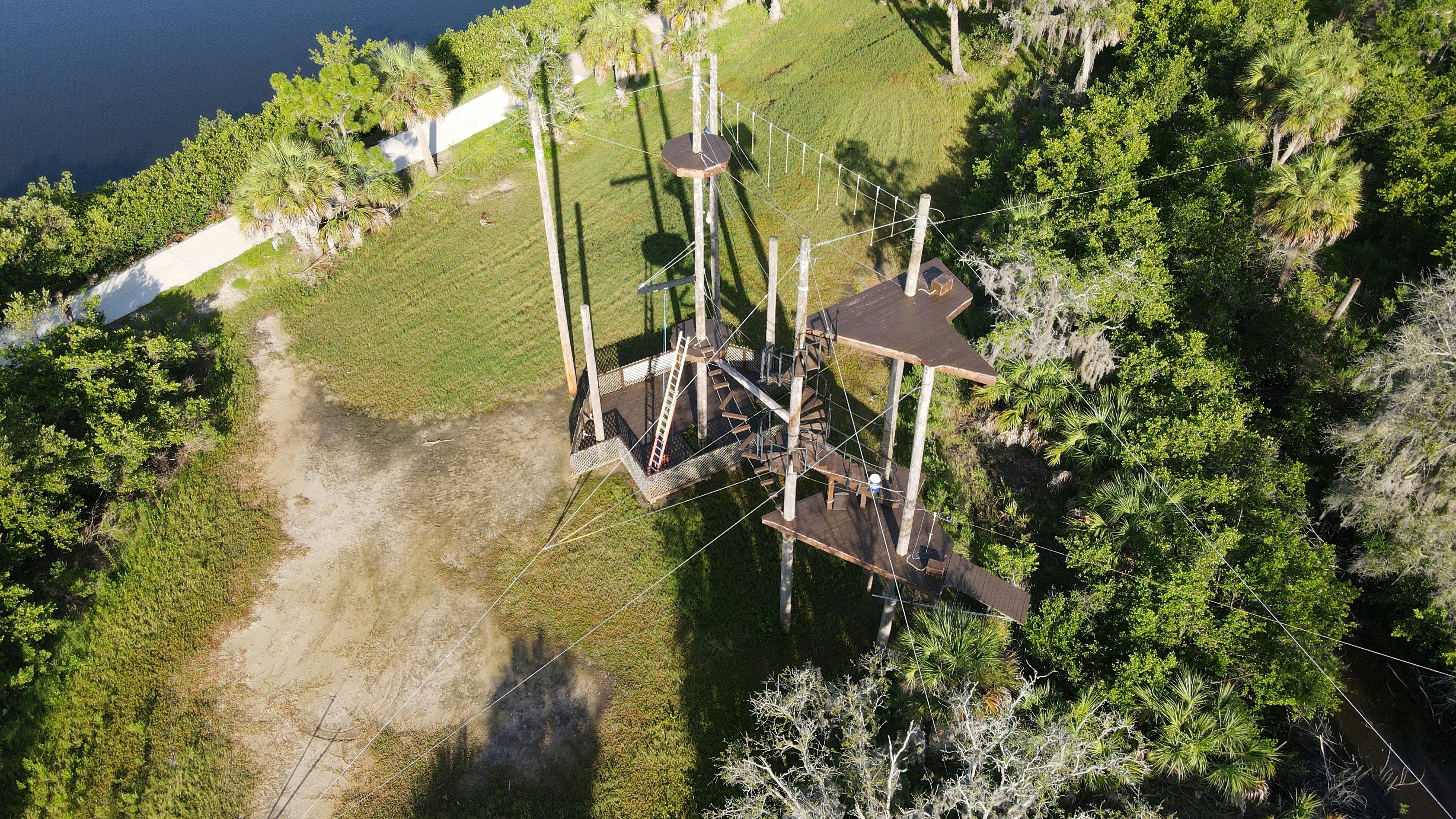 a wooden bridge over a river, A drone photo of zip line adventures in Tampa Bay, Florida. An aerial adventure and view of zip lining through the woods of Oldsmar, Florida.
