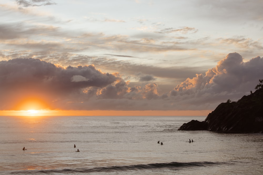 a group of people swimming in the water with a sunset in the background