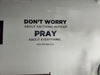 A wall has text painted on it that reads 'DON'T WORRY ABOUT ANYTHING: INSTEAD PRAY ABOUT EVERYTHING. PHILIPPIANS 4:6.' The text is in black and bold font on a light-colored background.