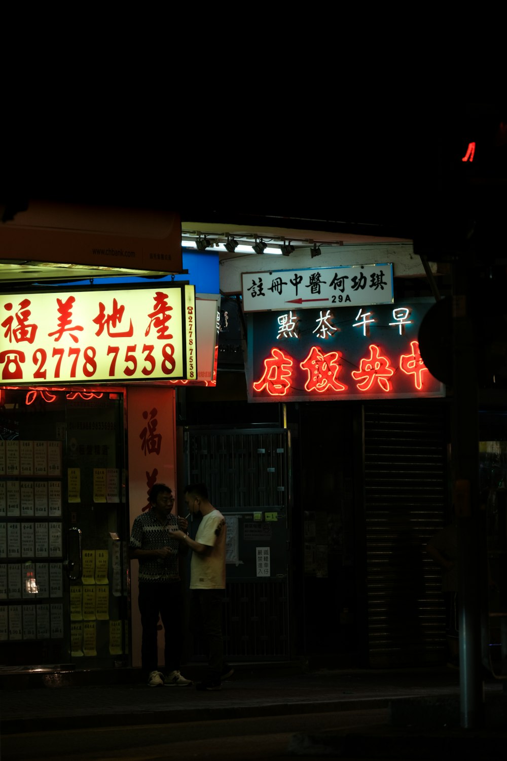 a couple of people standing in front of a store front with neon signs