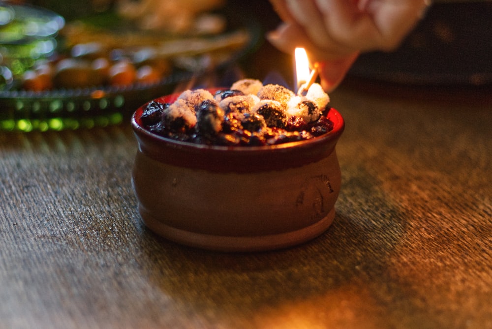 a hand lighting a candle in a bowl of ice cream