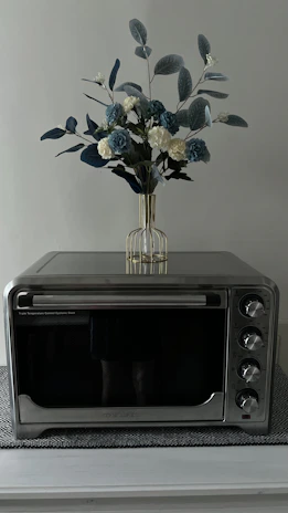 A shiny stainless steel microwave oven on a kitchen counter with fresh vegetables nearby.