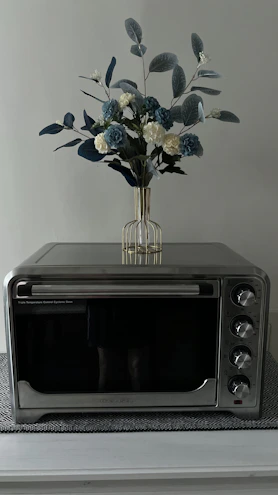A shiny stainless steel microwave oven on a kitchen counter with fresh vegetables nearby.