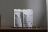 Minimalist flat lay of organic coffee seeds and elegant black packaging on a warm beige background.