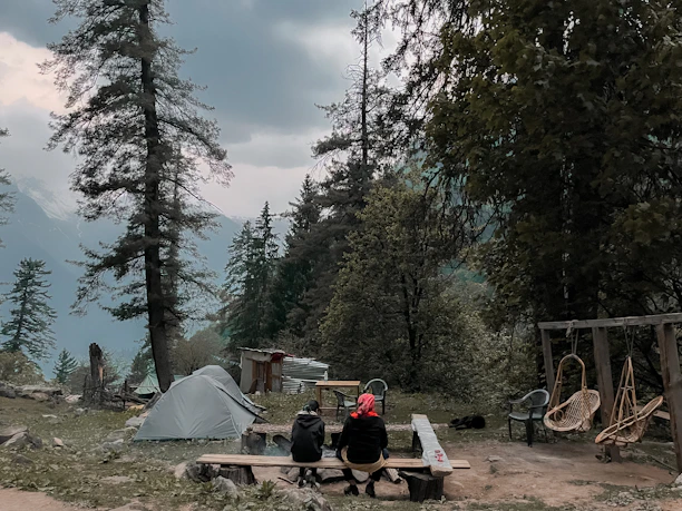A cozy campsite setup featuring Terraviva's folding metal chairs and a picnic table under tall pine trees.