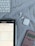 A tablet displaying mathematical problems is placed on a cloth surface. Nearby are a white stylus, a wireless keyboard, a pair of white wireless earbuds with their case, and a pink calculator.