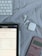 A tablet displaying mathematical problems is placed on a cloth surface. Nearby are a white stylus, a wireless keyboard, a pair of white wireless earbuds with their case, and a pink calculator.