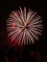 A spectacular fireworks display bursting in red, orange, and gold hues above a lively concert crowd.