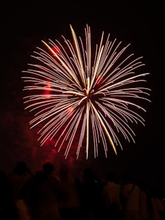 A vibrant burst of red and gold fireworks lighting up a dark night sky over a festive crowd.