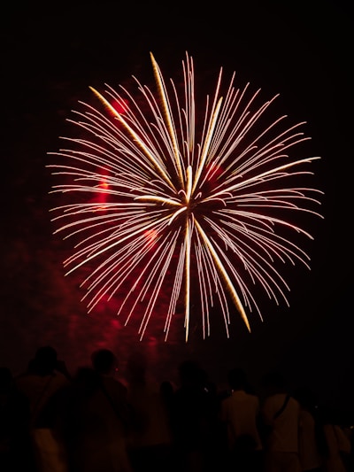A vibrant burst of red and gold fireworks lighting up a dark night sky over a festive crowd.