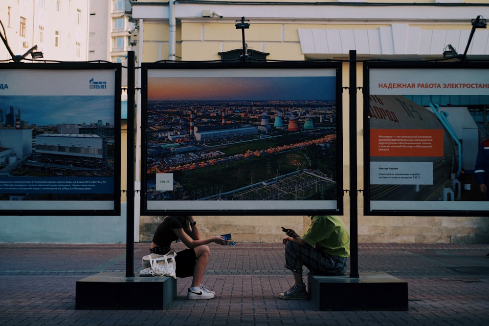 a couple of people sitting on a bench looking at a large screen