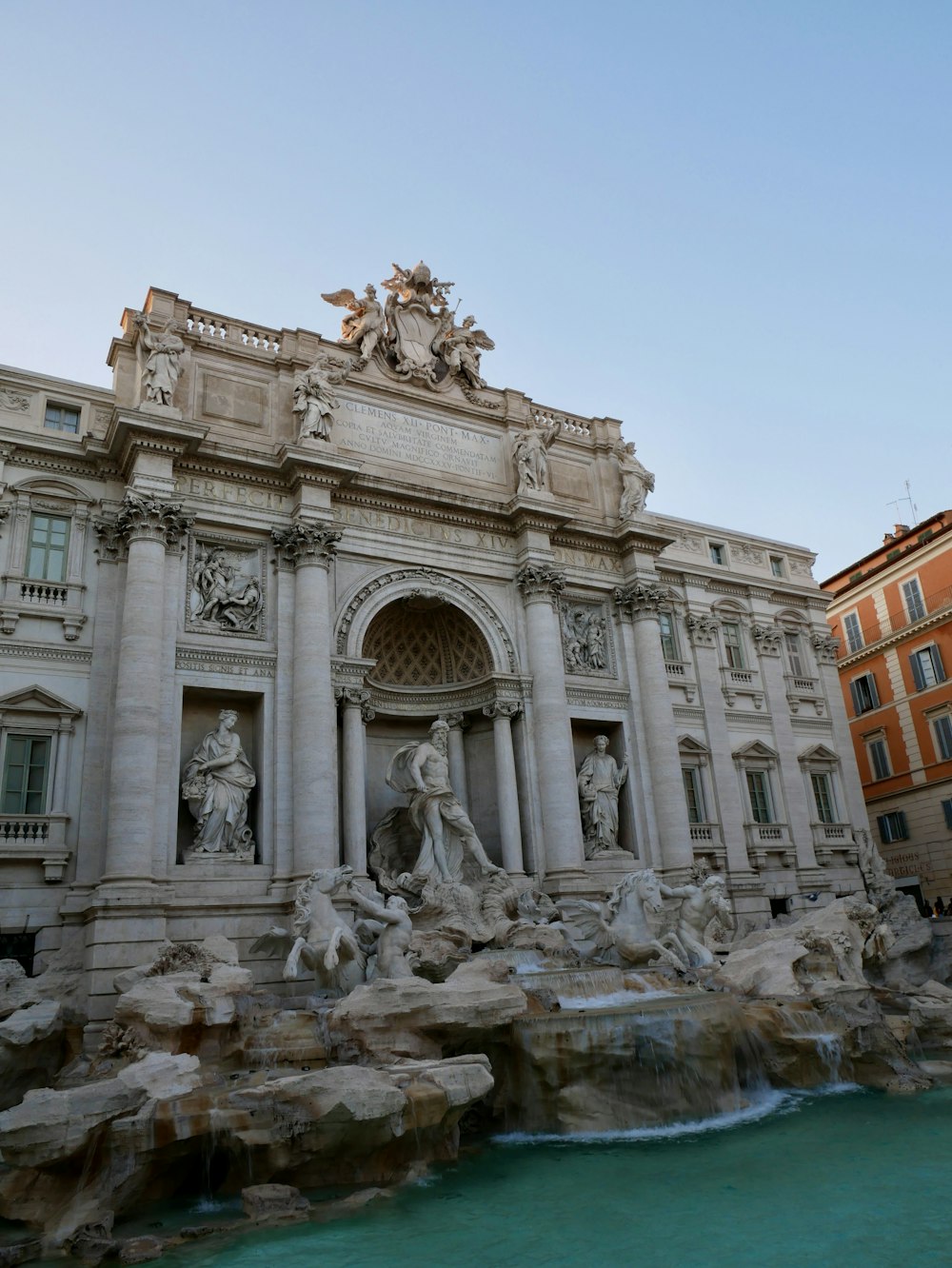 a large stone building with statues with Trevi Fountain in the background