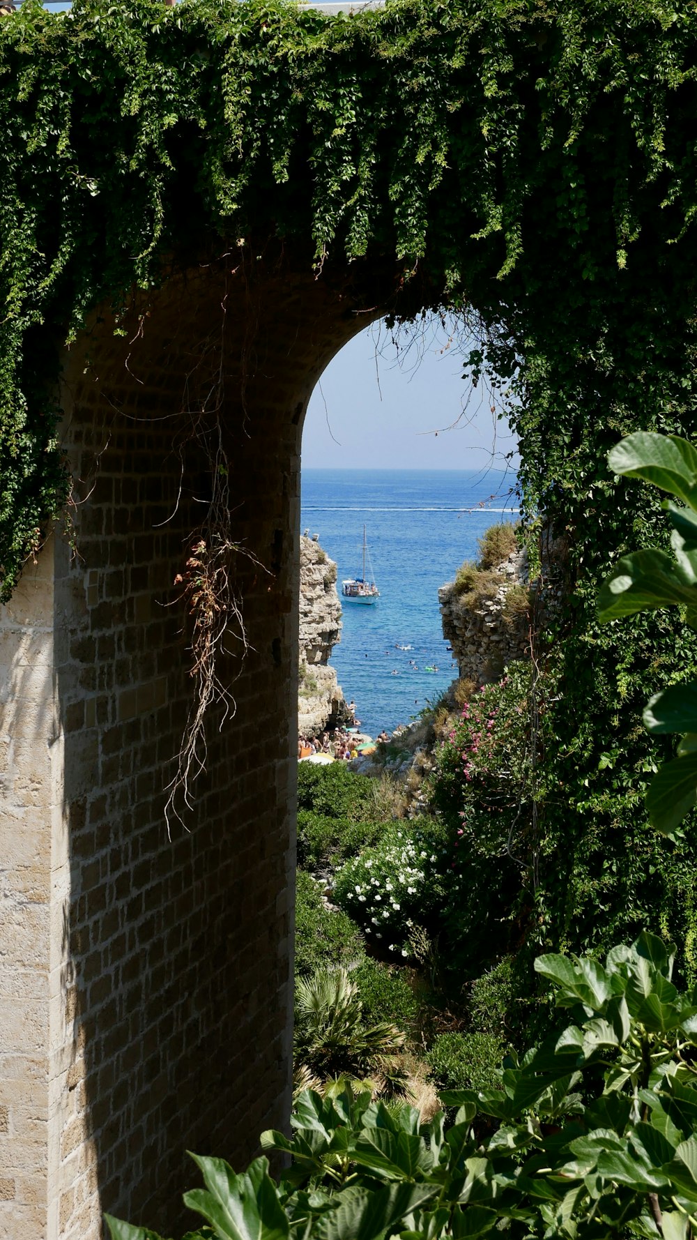 a brick archway with a boat in the water and a rocky beach