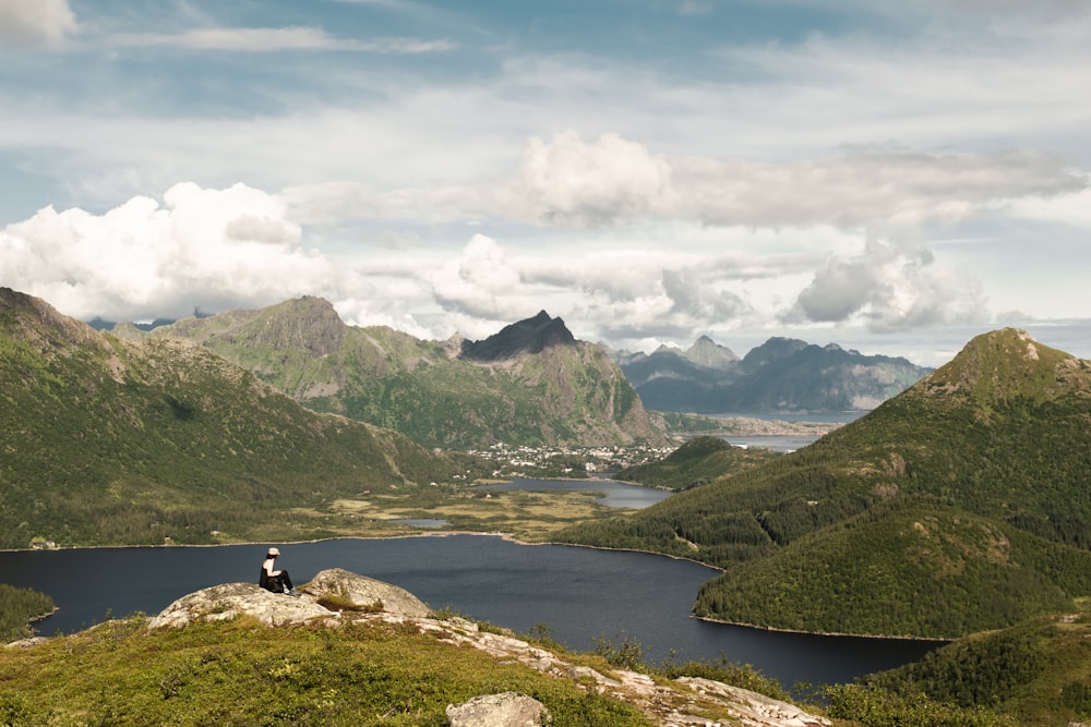 a person sitting on a rock by a body of water with mountains in the background