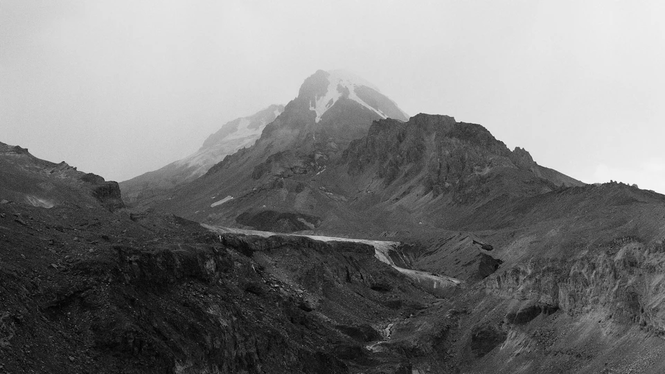 Mountain range with a dominant snow-capped peak in a vast, overcast landscape background