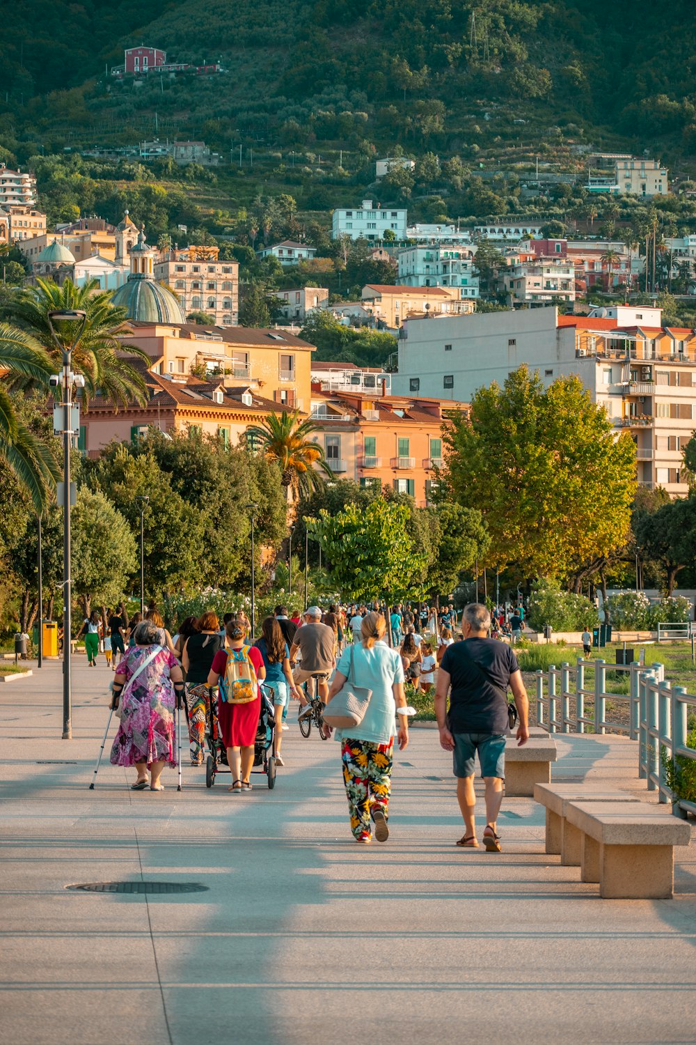 a group of people walking on a path with trees and buildings in the background