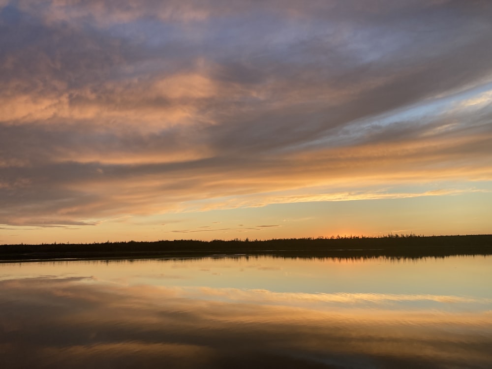 a body of water with trees and clouds in the sky