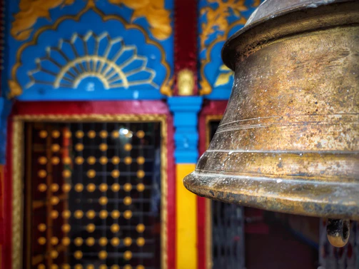 Close-up of a beautifully aged brass temple bell with intricate carvings hanging in a softly lit home mandir.