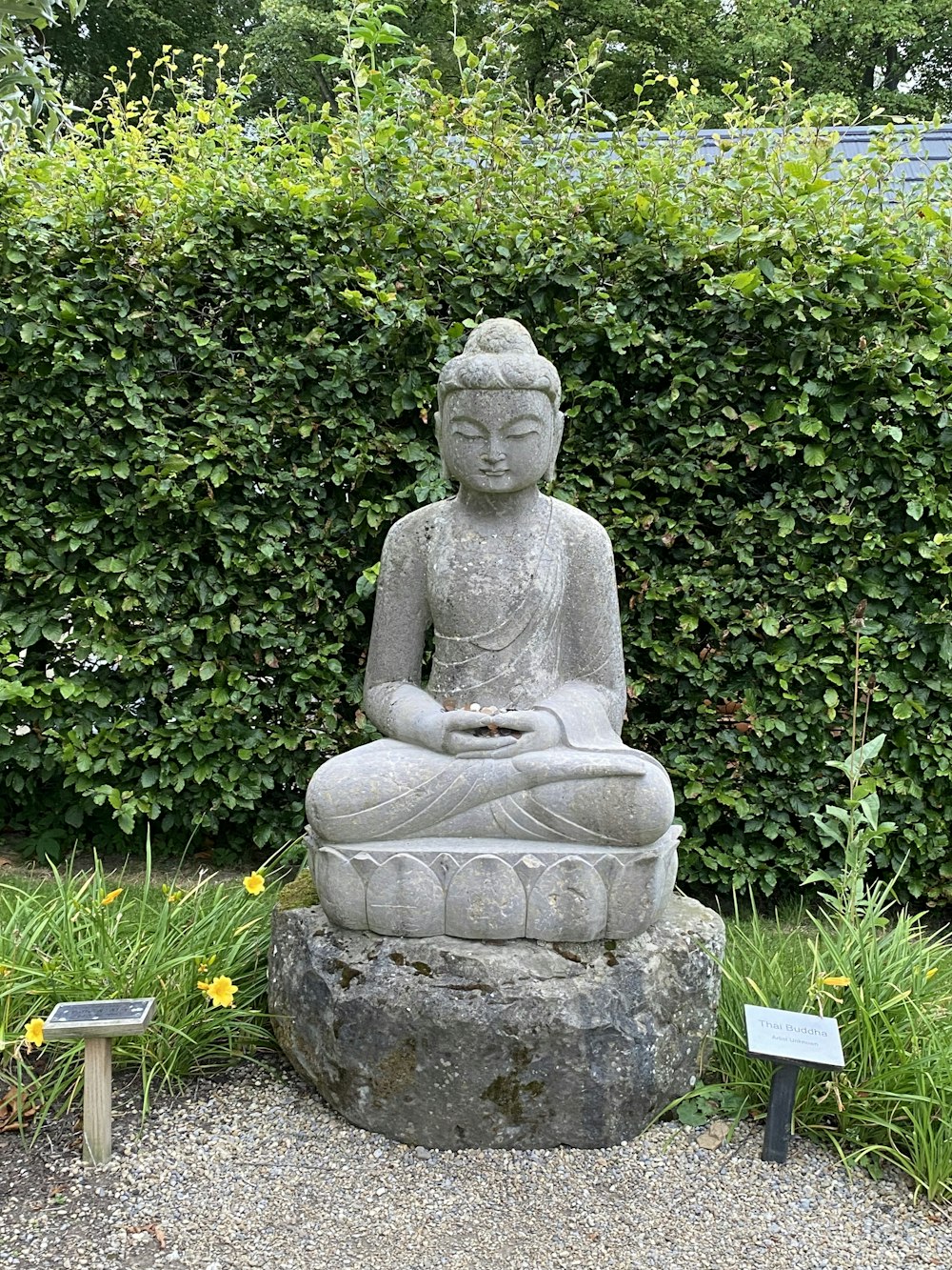 a statue of a person sitting on a rock in front of a hedge