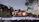 A modern house with a sloped red tile roof surrounded by lush green trees and landscaping. The house features large windows and a well-maintained garden area. A driveway leads up to the house with vintage-style street lamps lining the path.