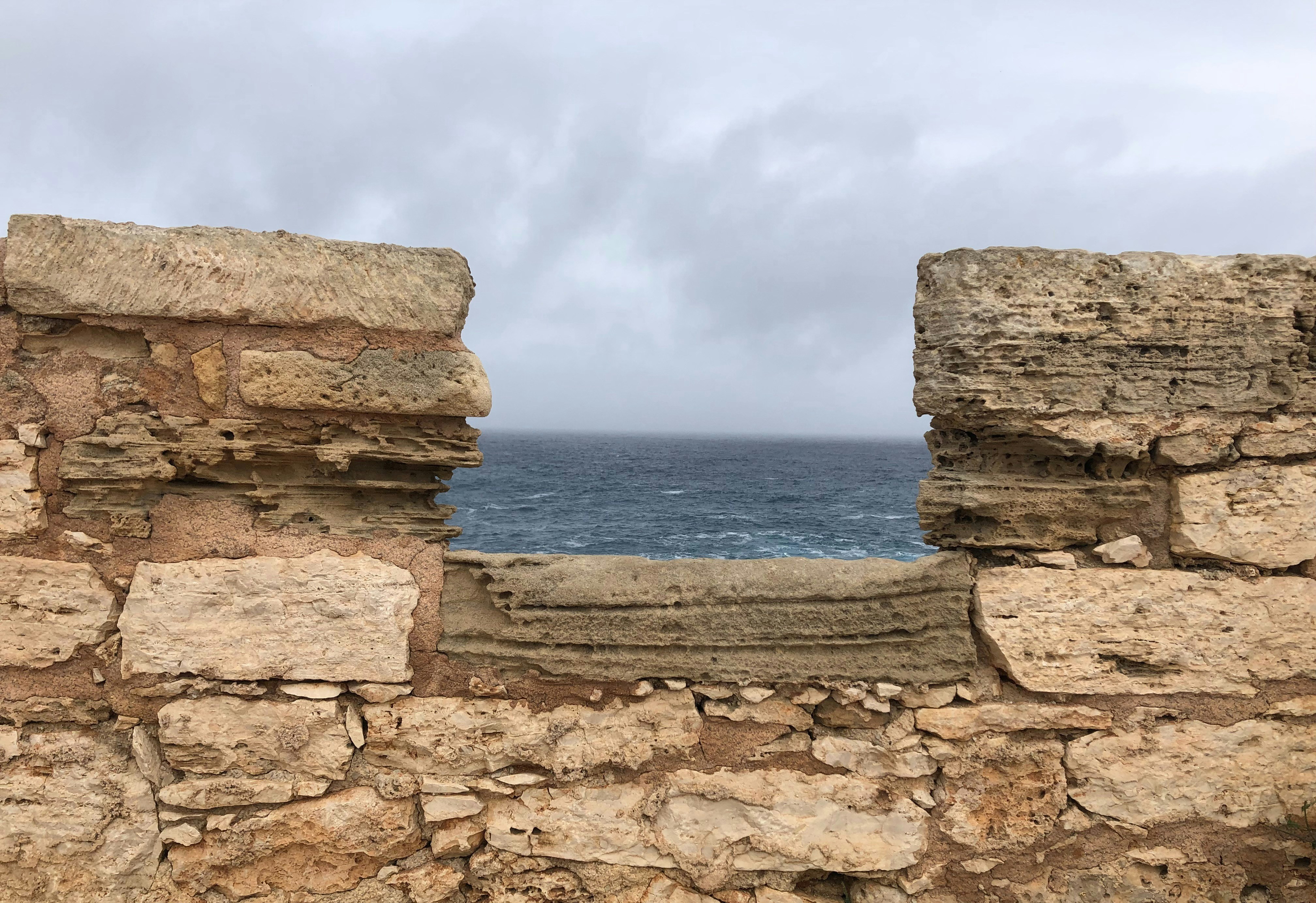 a stone wall with a view of the ocean and a cloudy sky
