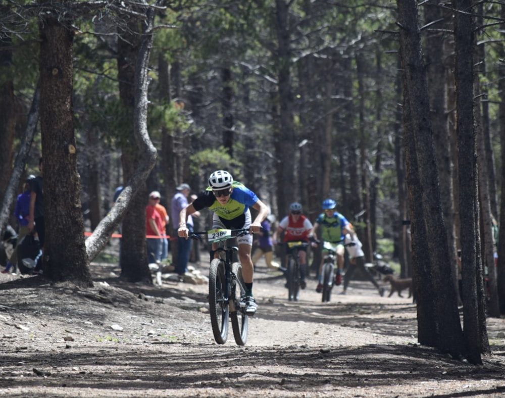 a group of people riding bikes on a dirt road in the woods