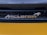 A close-up view of an automotive brand logo with a honeycomb grille pattern in the background. The logo appears metallic and reflective, positioned against a sleek, dark structure with a smooth, glossy yellow surface below.