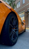 Close-up of a shiny orange sports car wheel on a dark street.